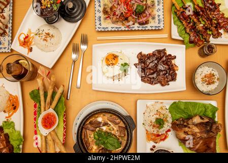 top view image of asian food dishes, tagalog, spring rolls, roast beef skewers with yakitori sauce, knuckle with rice, pork ceviche Stock Photo