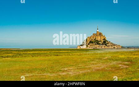 Stunning view of famous Le Mont Saint Michel tidal island on a bright sunny day with empty green fields, Normandy, Northern France Stock Photo