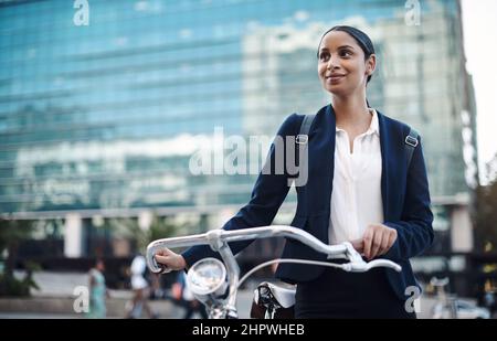 Welcome to the city, where opportunity awaits. Shot of a young businesswoman traveling with a bicycle through the city. Stock Photo