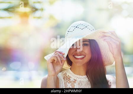 Protecting my skin against the summer sun. A happy young woman standing in the park wearing a sunhat. Stock Photo