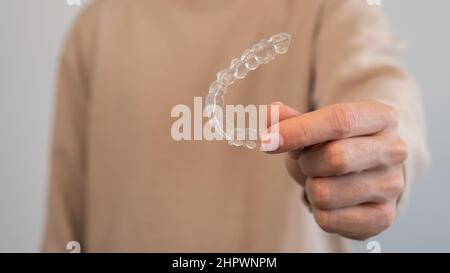 Caucasian young man showing an invisible silicone aligner for dental correction. Male hand holding the plastic braces dentistry retainers to straighte Stock Photo