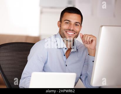 If you want the best then choose me. Portrait of a smiling young man sitting behind a computer screen. Stock Photo