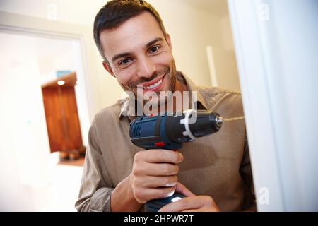 Hes handy to have around the house. Portrait of a smiling young man drilling a hole into the wall. Stock Photo