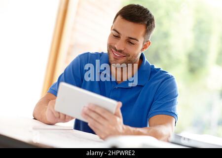 The tablet is one of his many business tools. Shot of a casual young man using a digital tablet at his desk. Stock Photo
