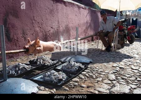 Pig on a spit being cooked on hot coals by a man at an event for family and friend in Trinidad, Cuba. Stock Photo