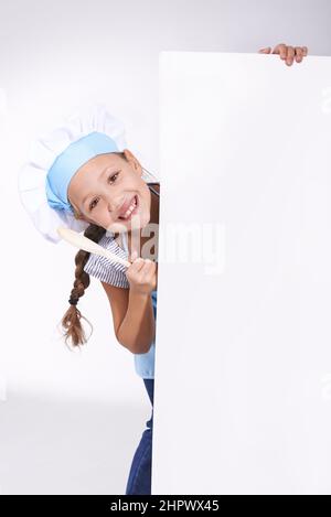 I love cooking.. Young girl wearing a chefs hat and holding a blank board reserved for copyspace. Stock Photo