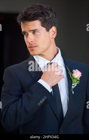 Looking great on his big day. A handsome groom wearing a pink rose on his jacket isolated on a black background. Stock Photo