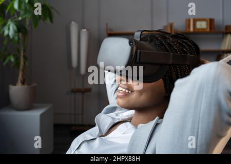 Relaxed lazy businesswoman wear virtual reality glasses watch movie at workplace procrastinating Stock Photo