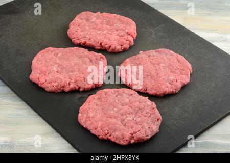 Raw formed ground beef hamburger patties on black cutting board Stock Photo