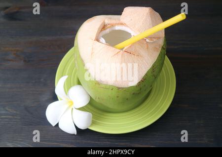 Fresh Young Coconut Juice with a Frangipani Flower on Black Wooden Backdrop Stock Photo