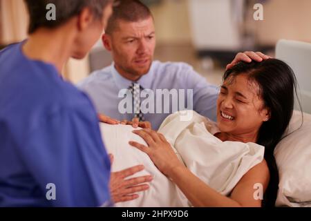 You are strong enough. Shot of a young woman giving birth with her husband supporting her in the background. Stock Photo