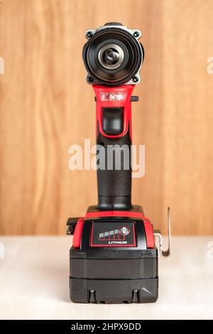 Cordless drill in black and red. A screwdriver with a drill lies on a wooden background. Modern carpentry tool close-up. Stock Photo
