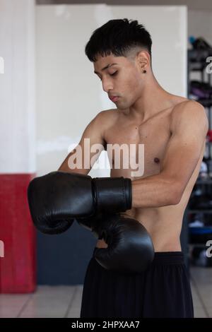 young mexican boxer with gloves on hitting the bag during his training inside the gymnasium Stock Photo