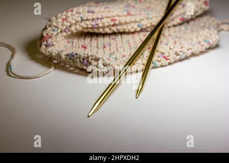 Close up defocused view of a hand knitted cotton wash cloth and a pair of metal knitting needles on white background, with copy space Stock Photo