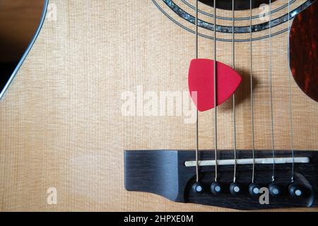 Red triangle guitar pick on an acoustic guitar Stock Photo