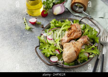 Healthy clean eating. Meat with fresh salad. Baked chicken drumsticks and a green vegan salad made from a of green leaves and spring vegetables on a s Stock Photo