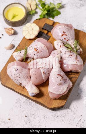 Chicken meat. Raw fresh chicken drumsticks with spices on a woden cutting board on a stone countertop. Stock Photo