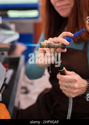 a woman working in her artisan jewelry workshop adjusting a torch to perform her work. Stock Photo