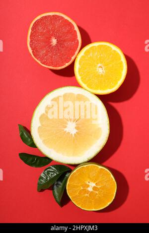 Citrus fruits halves with leaves on red background Stock Photo