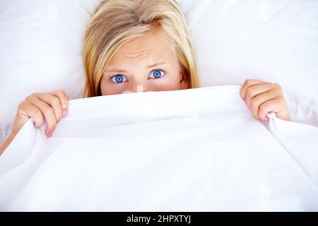 Something went bump in the night.... Young blonde woman covering half her face with a white sheet - portrait. Stock Photo
