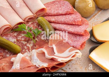 raw cheese in skillet and charcuterie on tiled table Stock Photo