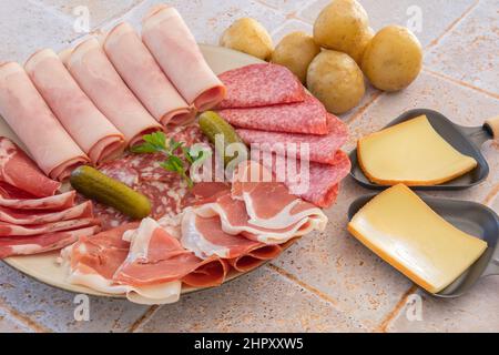 raw cheese in skillet and charcuterie on tiled table Stock Photo