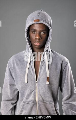 Serious African American male in hoodie standing and looking at camera against gray background in studio Stock Photo