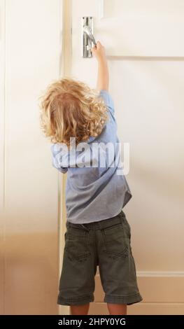 Help your child open the door to a promising future. Rear-view a toddler boy reaching up to open a door. Stock Photo