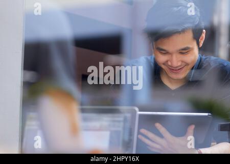 Relaxing in the internet cafe. Smiling Asian man using a digital tablet indoors. Stock Photo