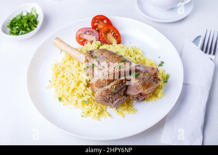 Lamb shin (shank) with rice, parsley, tomatoes and sauce on a white plate. Traditional dish. Close-up, selective focus. Stock Photo