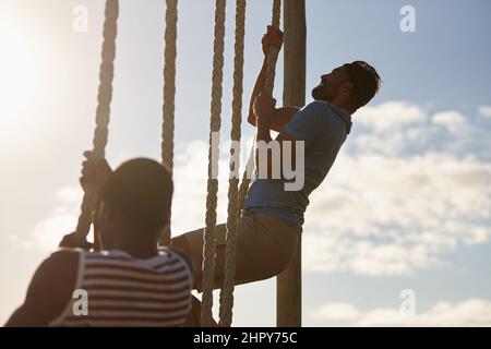 Mind over matter. Shot of two young men climbing up ropes at a military bootcamp. Stock Photo