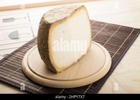 Sardo cheese on a wooden plate. Hard grating cow cheese. Stock Photo