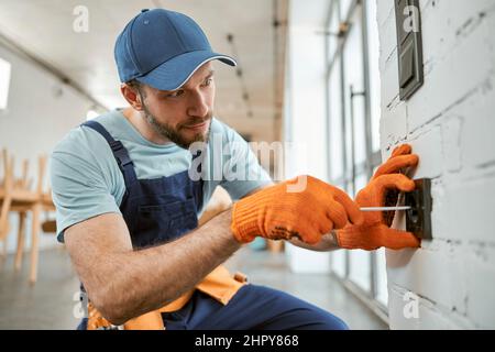 Bearded man fixing electrical wall socket with screwdriver Stock Photo