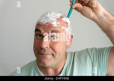 Closeup of a middle-aged Caucasian man shaving his head with a razor Stock Photo