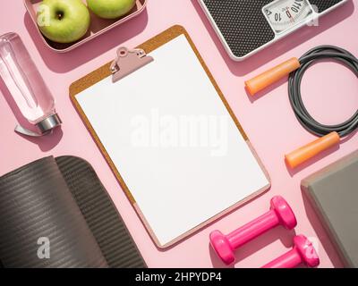 Stylish workout plan mockup in gray and pink colors. Fitness training flat lay. Top view of sport equipment, water bottle, scales and empty white sheet on clipboard on pink background. Copy space Stock Photo