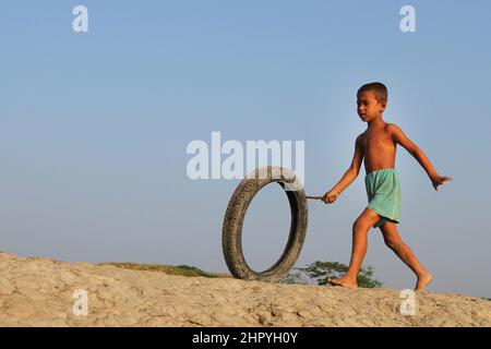 Khulna, Bangladesh - October 08, 2014: A child plays with a motorcycle tire in the coastal area of Khulna in Bangladesh. Stock Photo