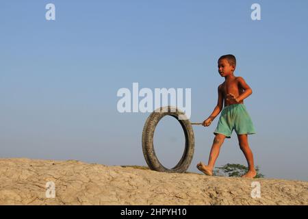 Khulna, Bangladesh - October 08, 2014: A child plays with a motorcycle tire in the coastal area of Khulna in Bangladesh. Stock Photo