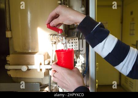 A woman's hand pouring boiling water into a red glass in a train car. Stock Photo