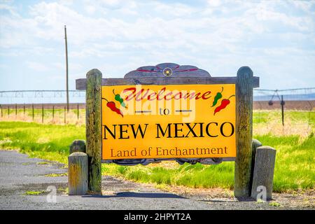 Rustic wooden roadside sign - Welcome to New Mexico Land of Enchantment with rolling irrigation system blurred in field behind Stock Photo