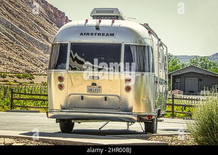 2021 06 04 Grand Junction Colorado USA - Airstream camper trailer parked on concrete with grape vineyards and mesa and barn behind it. Stock Photo