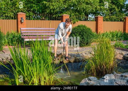 man cleans garden pond bottom with high-pressure washer from mud and sludge. Stock Photo