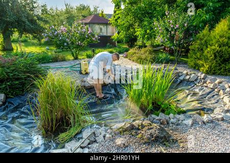 man cleans garden pond bottom with high-pressure washer from mud and sludge. Stock Photo