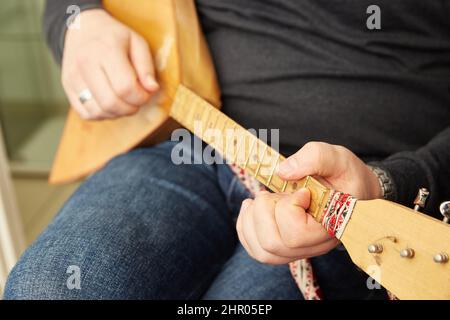 Men's hands play the balalaika, a Russian folk stringed plucked musical instrument with a triangular-shaped body having three strings Stock Photo