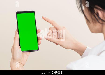 Woman using smartphone with blank green screen chromakey background. Rear view Stock Photo