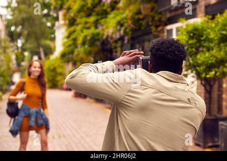 Woman Posing And Man Taking Photos On Camera As Young Couple Travel Through City Together Stock Photo