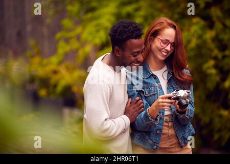 Couple In City Taking Photo On Retro Film Camera To Post To Social Media Stock Photo