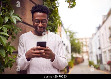 Male Vlogger Or Social Influencer In City Using Mobile Phone On Street To Post To Social Media Stock Photo