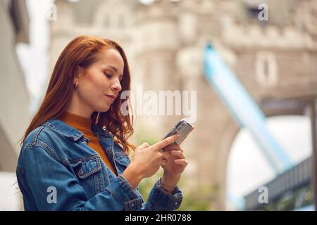 Female Vlogger Or Social Influencer Travelling Through London Using Mobile Phone By Tower Bridge Stock Photo