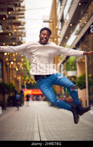 Portrait Of Young Man Enjoying City Life Jumping In Air Heading For Night Out Stock Photo