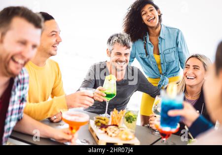 Friends toasting fancy colored drinks at open air cocktail bar terrace - Life style concept with young people having fun together sharing cocktails on Stock Photo